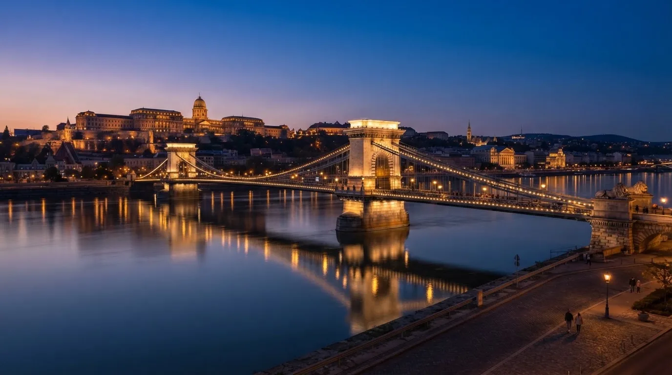 A budapesti Lánchíd esti fényekben a Duna fölött, a háttérben a budai Vár, forgalom nélküli rakpart.